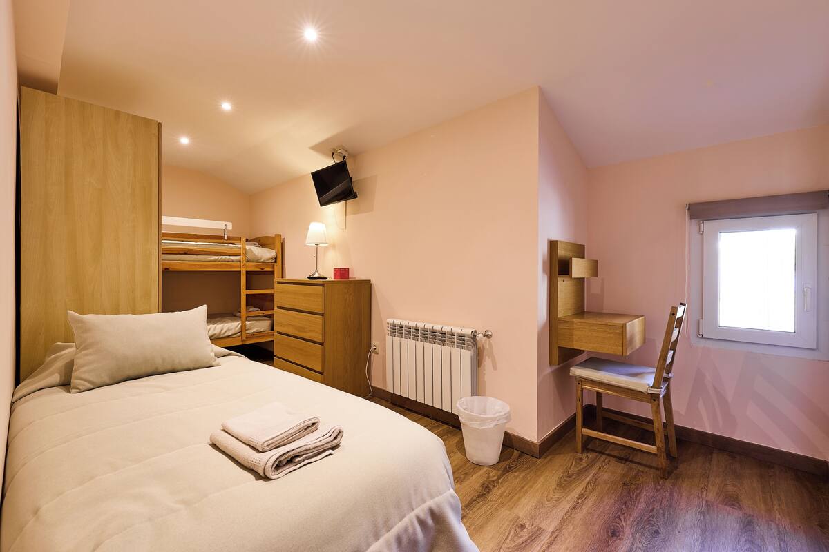Ein Schlafzimmer mit einem Bett, einer Holzkommode, einem Schreibtisch mit Stuhl, einem Heizkörper und einem an der Wand befestigten Fernseher.