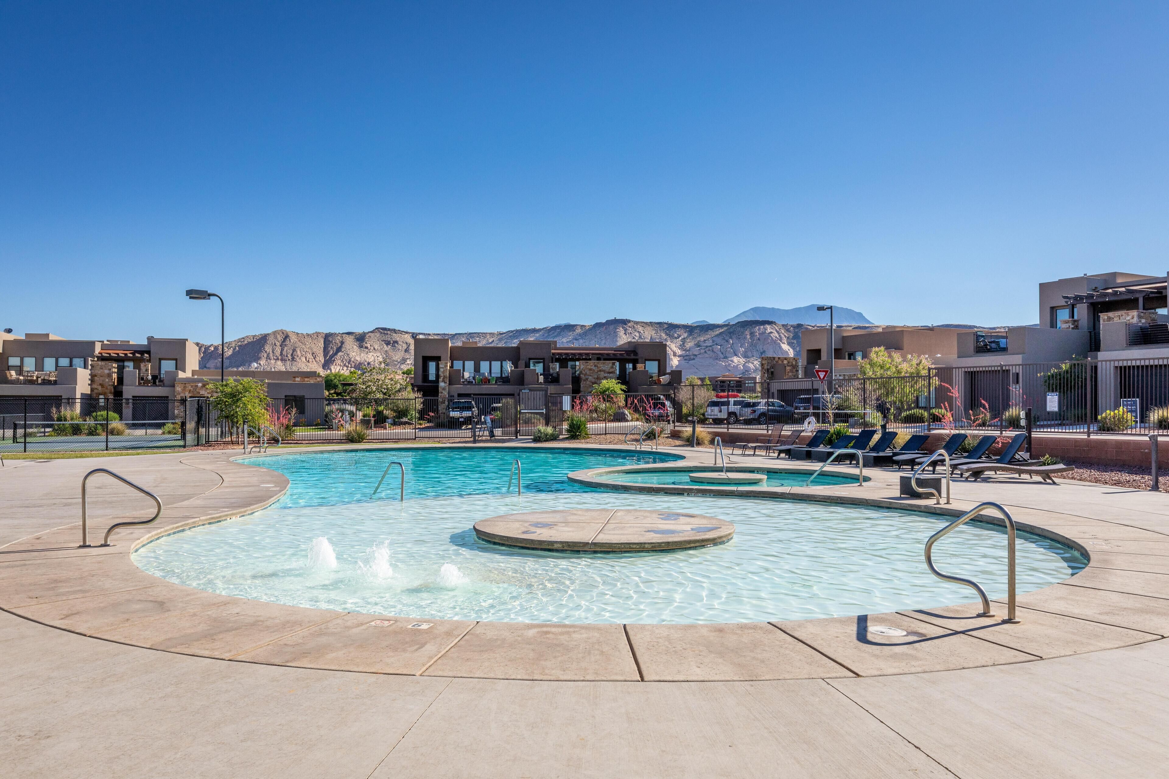 A swimming pool with multiple lanes and a surrounding deck area, set against a backdrop of mountains and modern buildings.