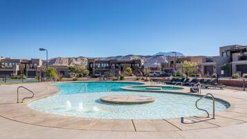 A swimming pool with multiple lanes and a surrounding deck area, set against a backdrop of mountains and modern buildings.