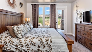 A bedroom with a bed, a wooden headboard, a ceiling fan, a TV, and a view of the outdoors. - Stay On Course (St. George)