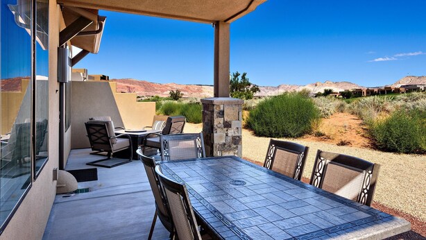 An outdoor patio with a table and chairs, a stone pillar, and a view of a desert landscape. - Stay On Course (St. George)