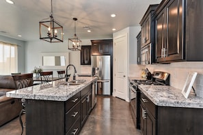 A modern kitchen with dark cabinetry, granite countertops, stainless steel appliances, and pendant lighting.