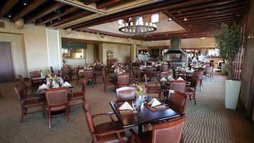 A spacious dining area with multiple tables and chairs, a central chandelier, and a large plant.