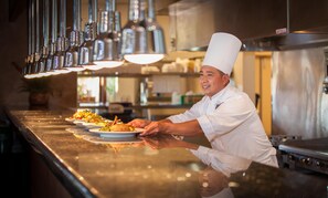A chef in a professional kitchen environment, serving food on a tray. - Kickin' It At Karisma (St. George)