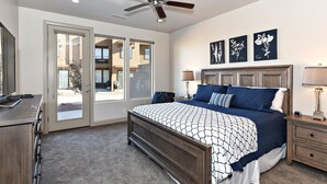A bedroom with a bed, a ceiling fan, a nightstand, a lamp, and a door leading to an outdoor area. - Red Rock Retreat (St. George)
