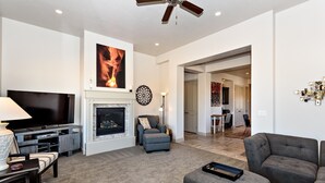 A living room with a fireplace, a television, and a ceiling fan. - Red Rock Retreat (St. George)
