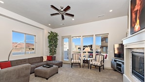 A living room with a sectional sofa, ottoman, chairs, a fireplace, and a ceiling fan. - Red Rock Retreat (St. George)