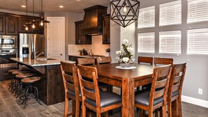 A kitchen with a central island, wooden chairs, a dining table, and bar stools. - Paradise Found (St. George)