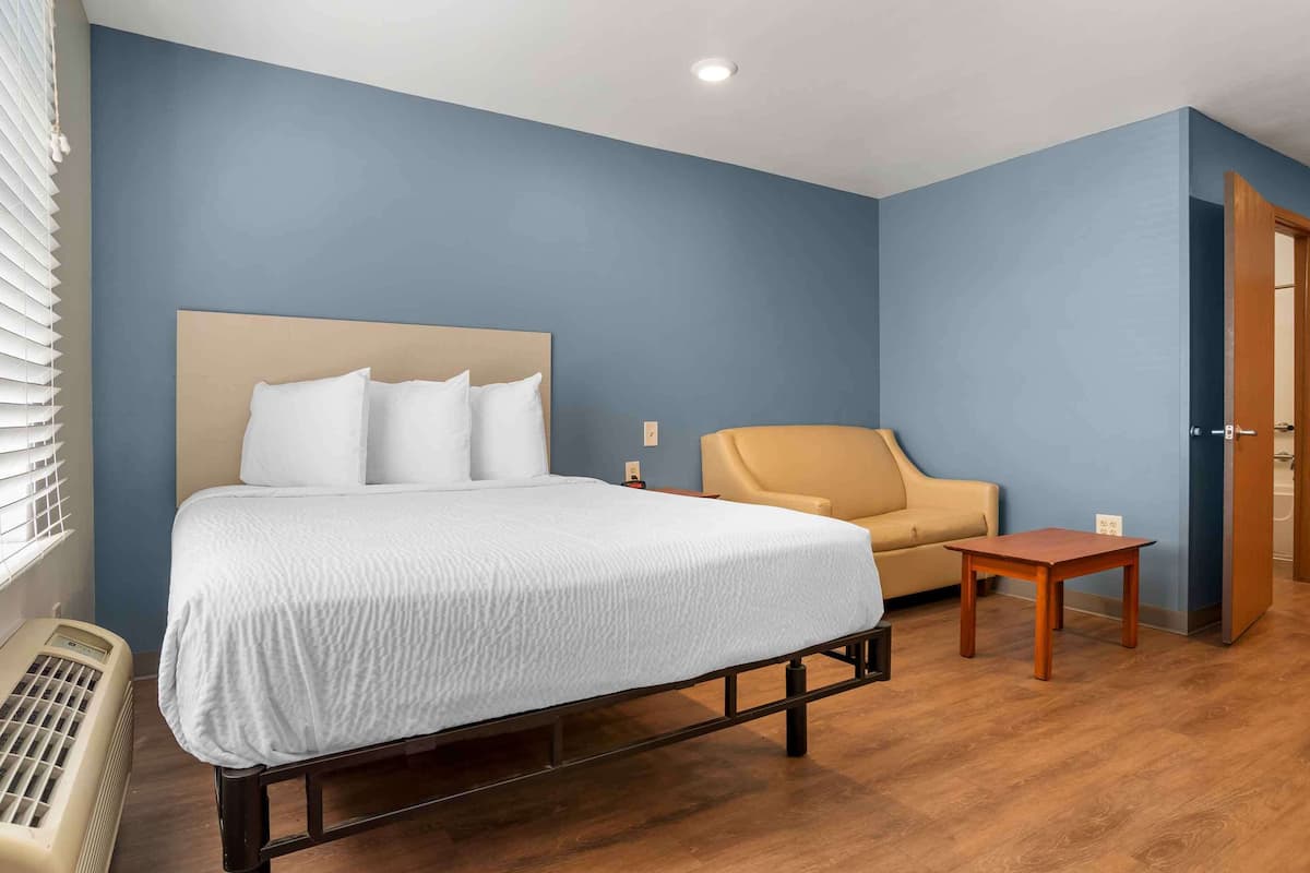 A hotel room with a bed, a chair, a small table, and a heater.