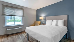 Een moderne hotelkamer met een groot bed, een stoel, een bureau met lamp en een raam met zonwering.