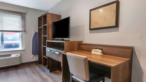 Een hotelkamer met een houten bureau, een televisie, een stoel, een kledingkast en een raam met jaloezieën.
