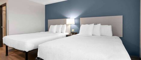 A hotel room with two beds, a nightstand with a lamp, and a door.