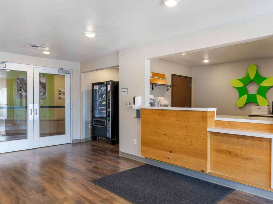 A reception area with a wooden counter, glass doors, and a green logo on the wall.