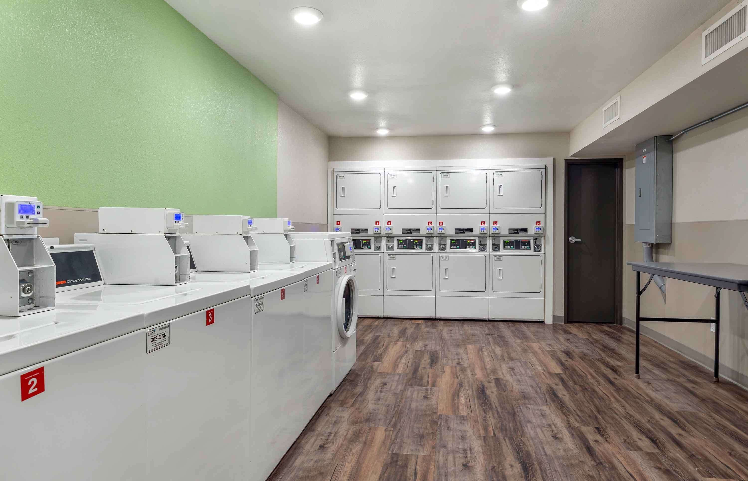 A laundry facility with multiple washing machines and dryers, a table, and a door.