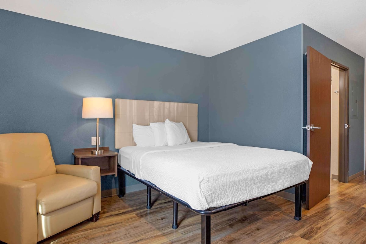 A hotel room with a bed, a chair, a nightstand, and a lamp.