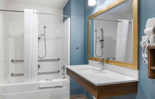 A bathroom with a shower, a sink, a mirror, and a hairdryer.