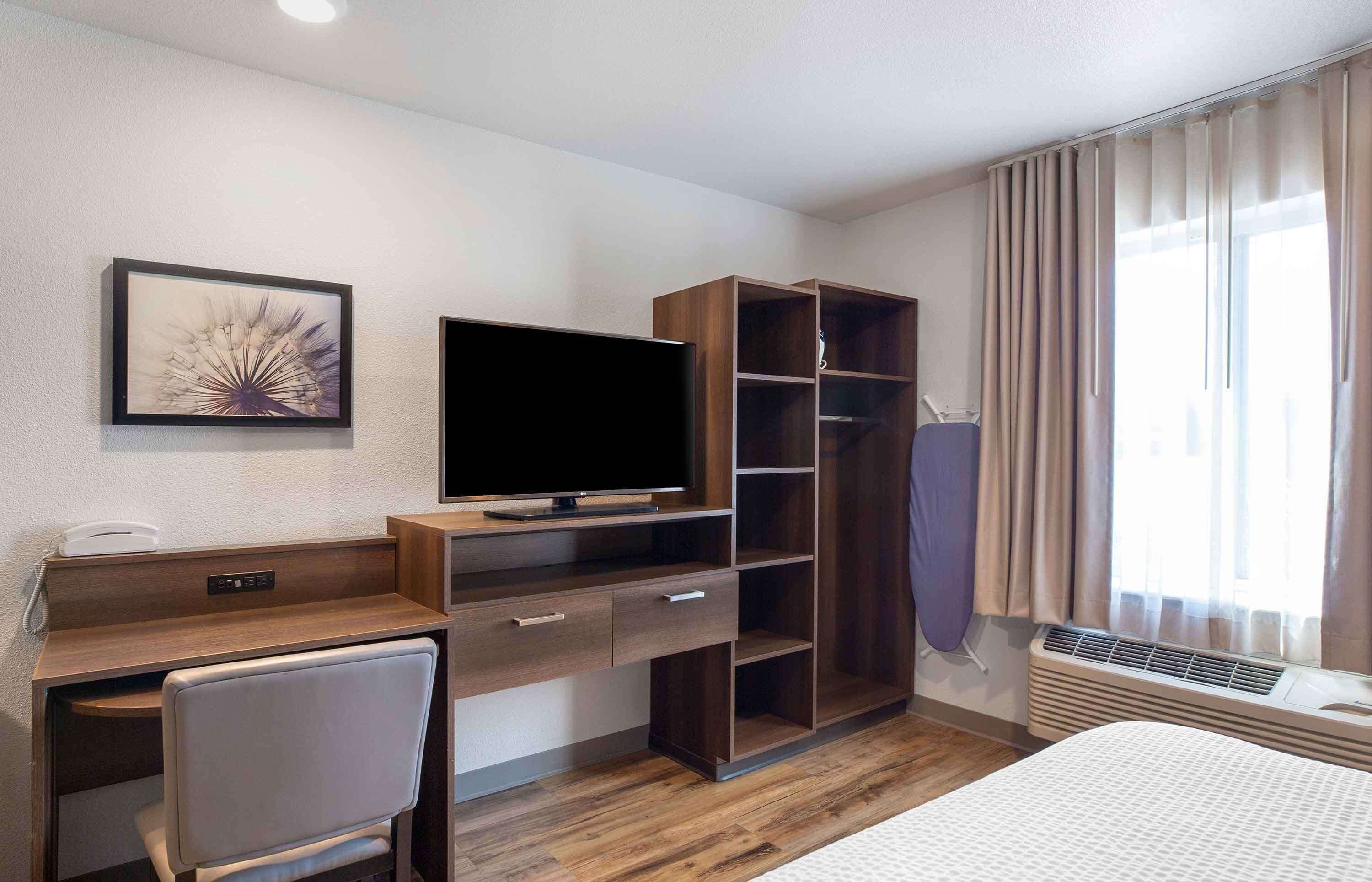 A hotel room with a bed, a desk with a chair, a television, a wardrobe, and a window with curtains.