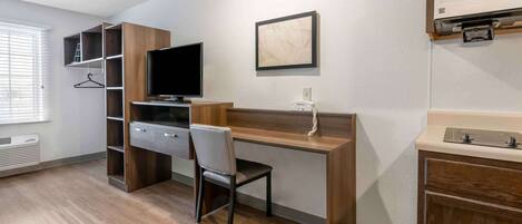 Habitación de hotel moderna con un escritorio de madera, televisor, silla, armario y tocador en el baño.