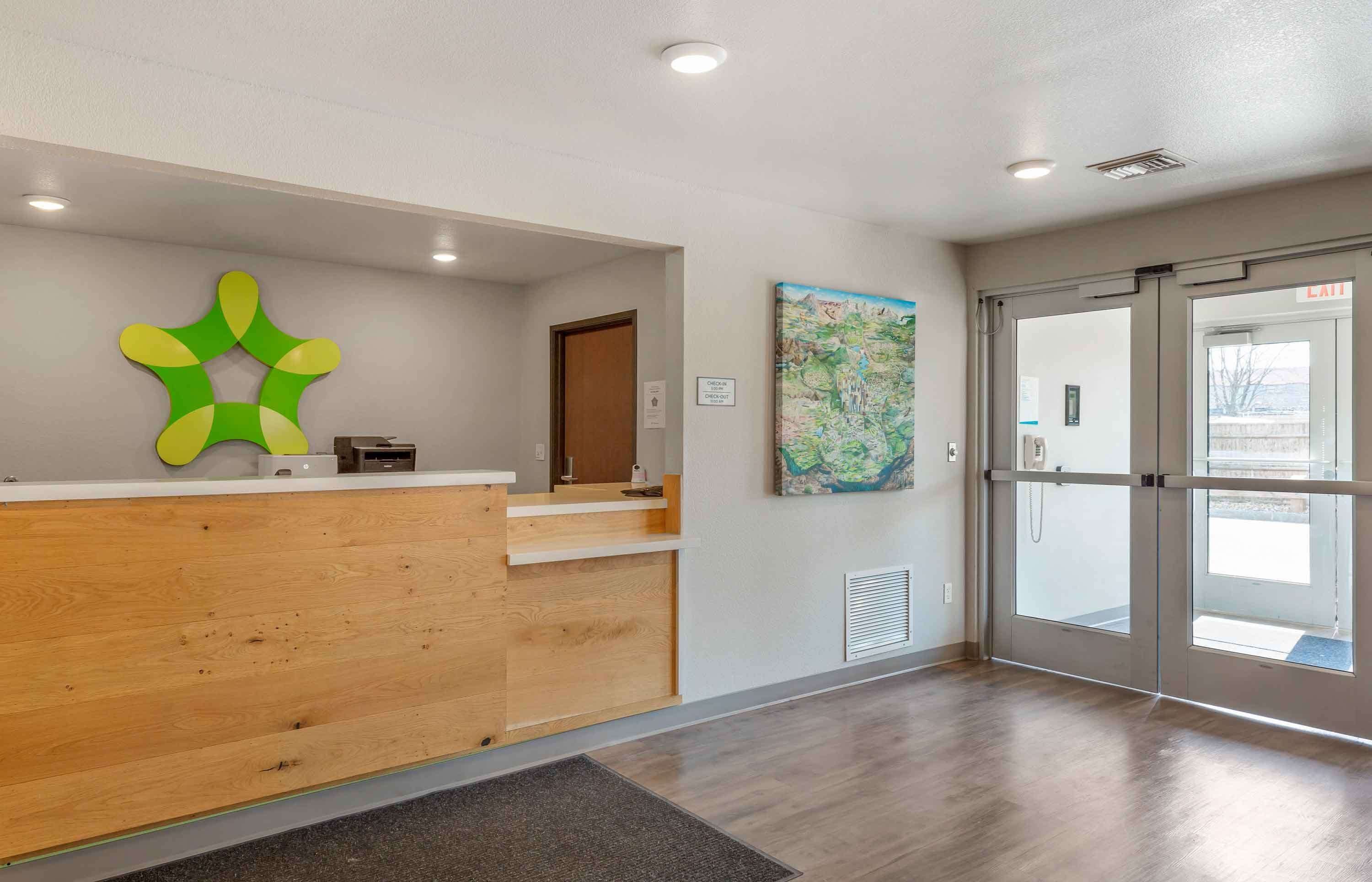 Un área de recepción con mostrador de madera, una obra de arte abstracta verde, un mapa en la pared y una puerta de cristal que da al exterior.