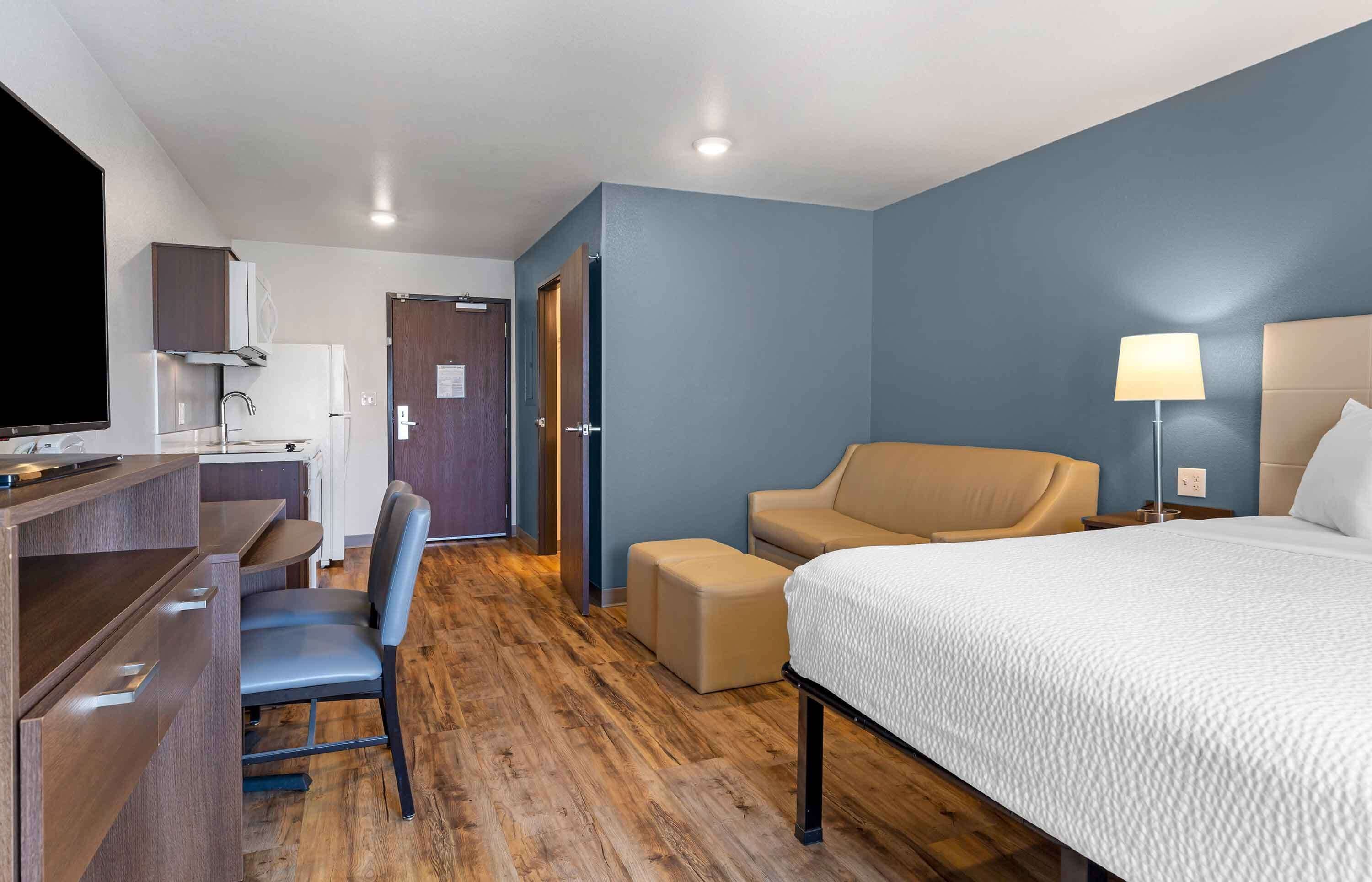 A hotel room with a bed, a desk with a chair, a sofa, and a TV.