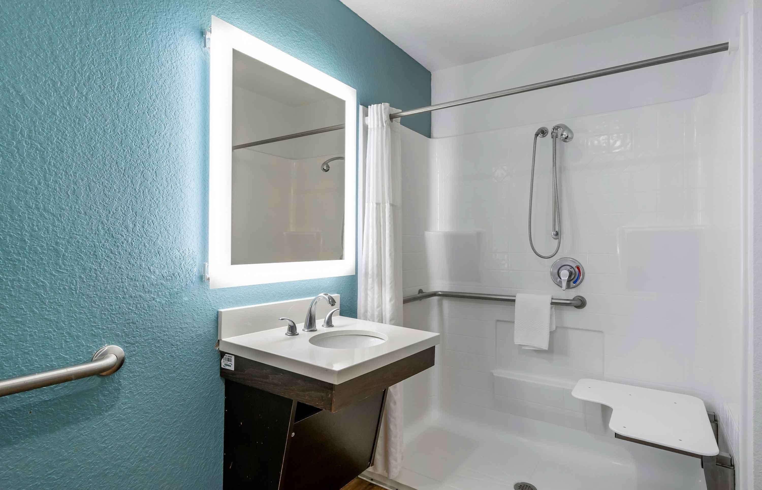 A bathroom with a white sink, a mirror, a shower with a handheld showerhead, and a towel rack.