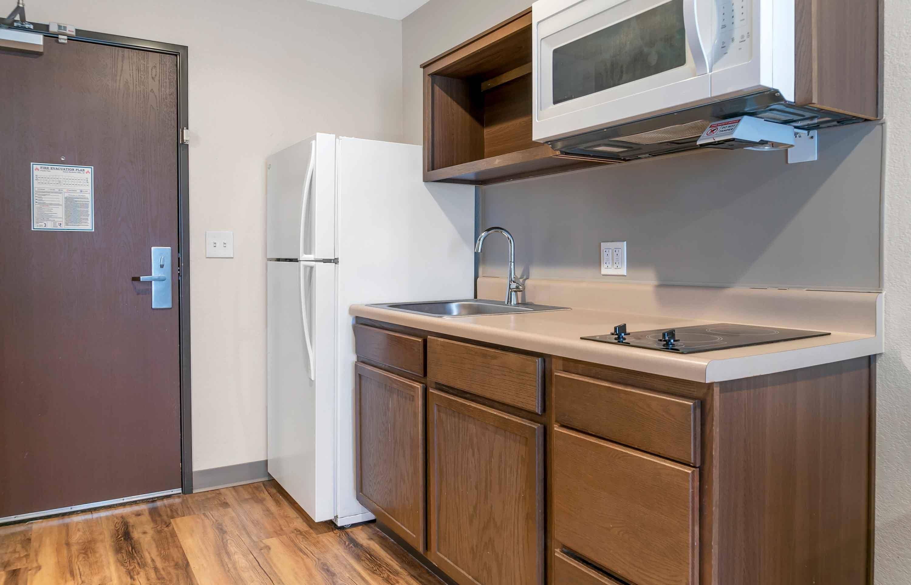 Una cocina compacta con refrigerador, microondas, lavamanos y armarios de madera.