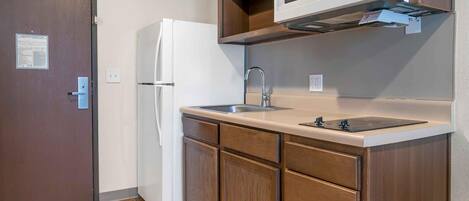 A compact kitchen with a refrigerator, microwave, sink, and wooden cabinets.