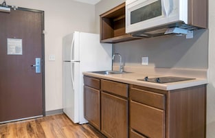 Una cocina compacta con refrigerador, microondas, lavamanos y armarios de madera.