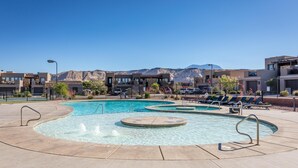 A swimming pool with multiple lanes and a surrounding deck area, set against a backdrop of mountains and modern buildings. - 18th Fairway to Heaven (St. George)