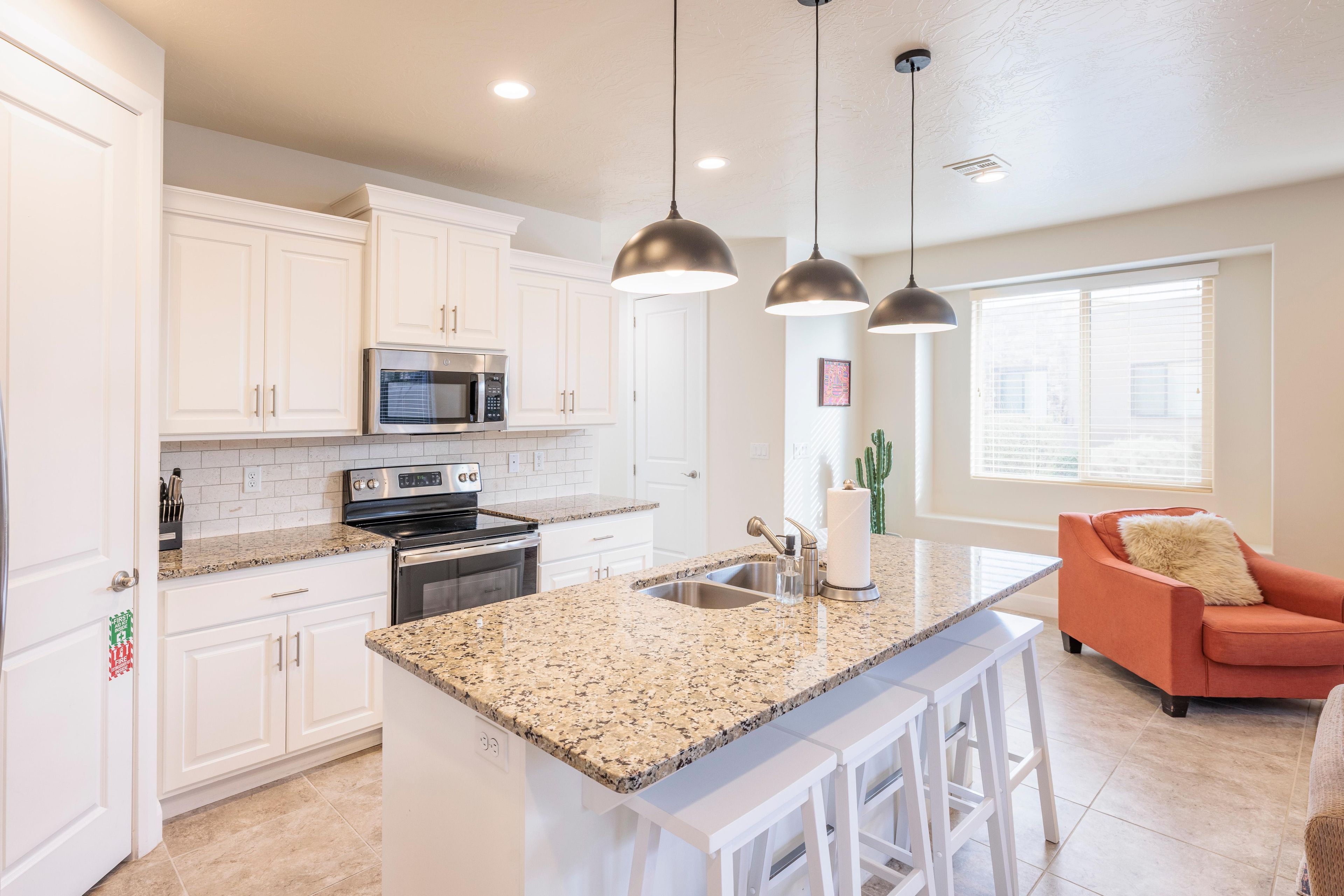 A modern kitchen with white cabinets, granite countertops, stainless steel appliances, and pendant lighting.