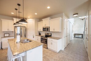 A modern kitchen with white cabinetry, granite countertops, stainless steel appliances, and pendant lighting.