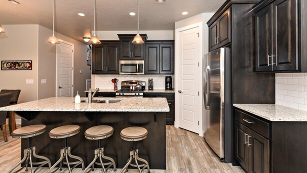 A modern kitchen with dark cabinets, stainless steel appliances, and a central island with stools. - High Desert Hideaway (St. George)