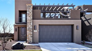 A modern two-story house with a garage, a stone pillar, and a pergola with solar panels. - The Painted Horse (St. George)