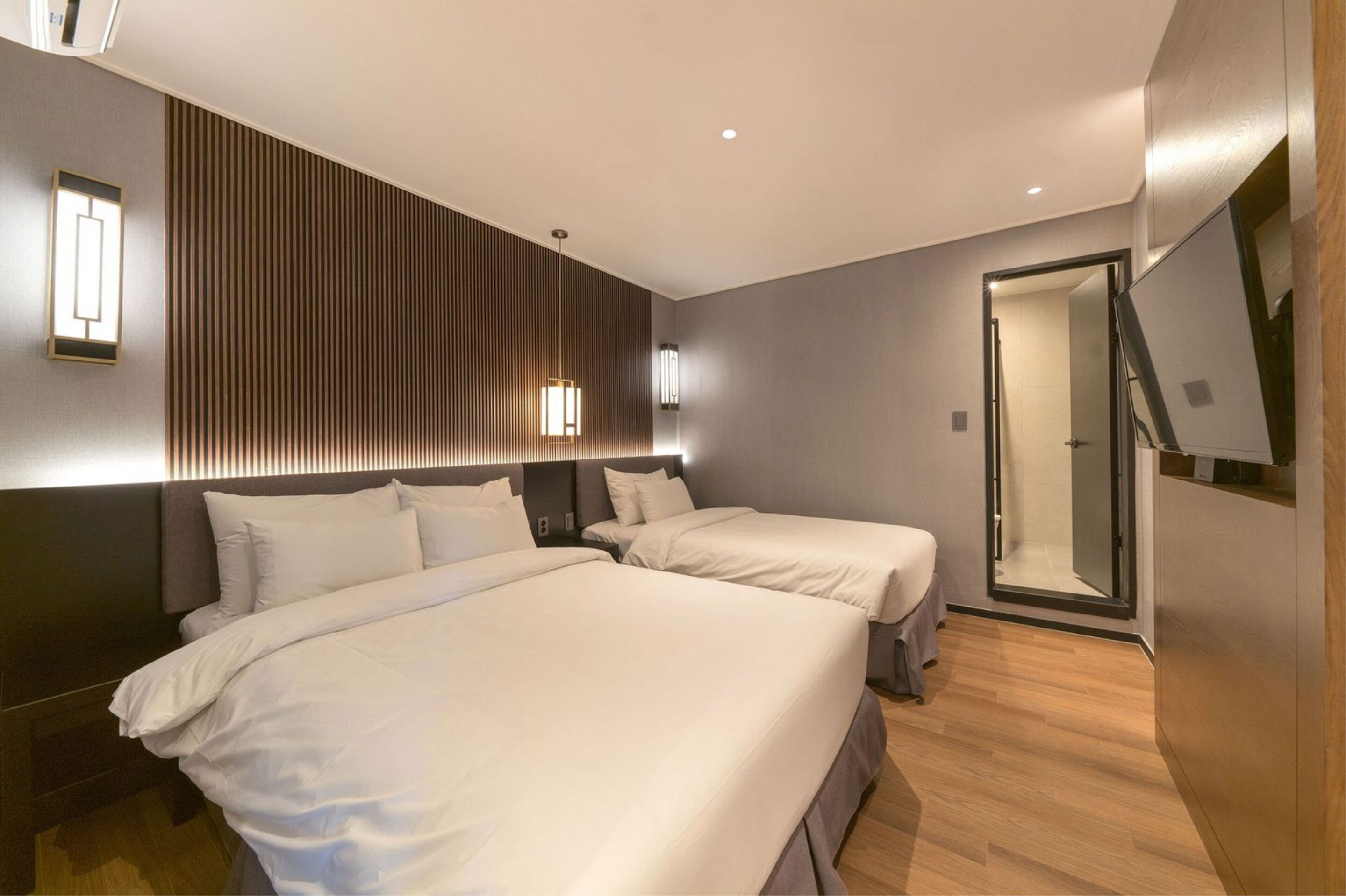 A modern hotel room with two beds, a large mirror, and a wooden floor.