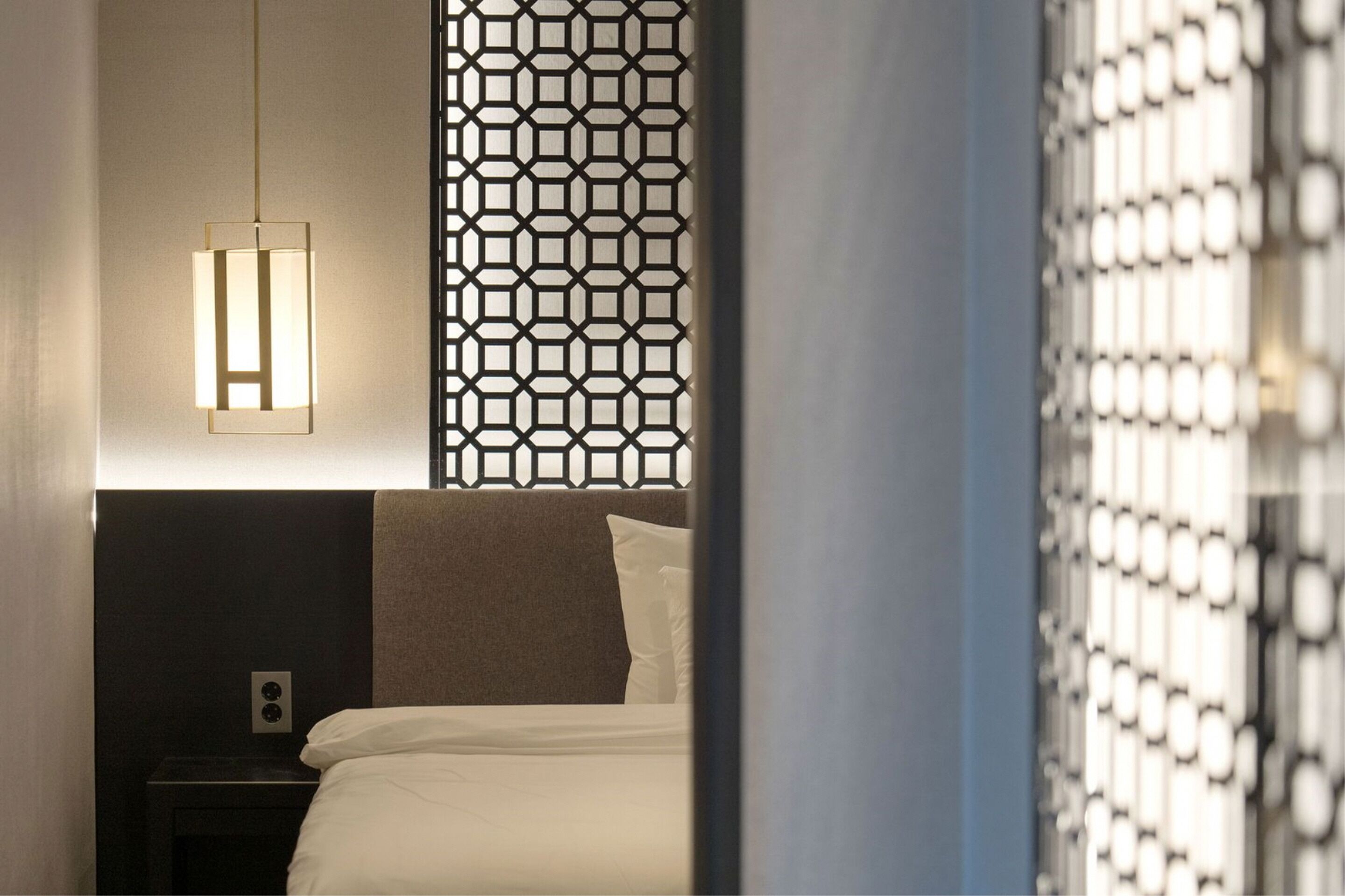 Et hotelværelse med seng, et natbord, en vægmonteret lampe og en dekorativ panel.