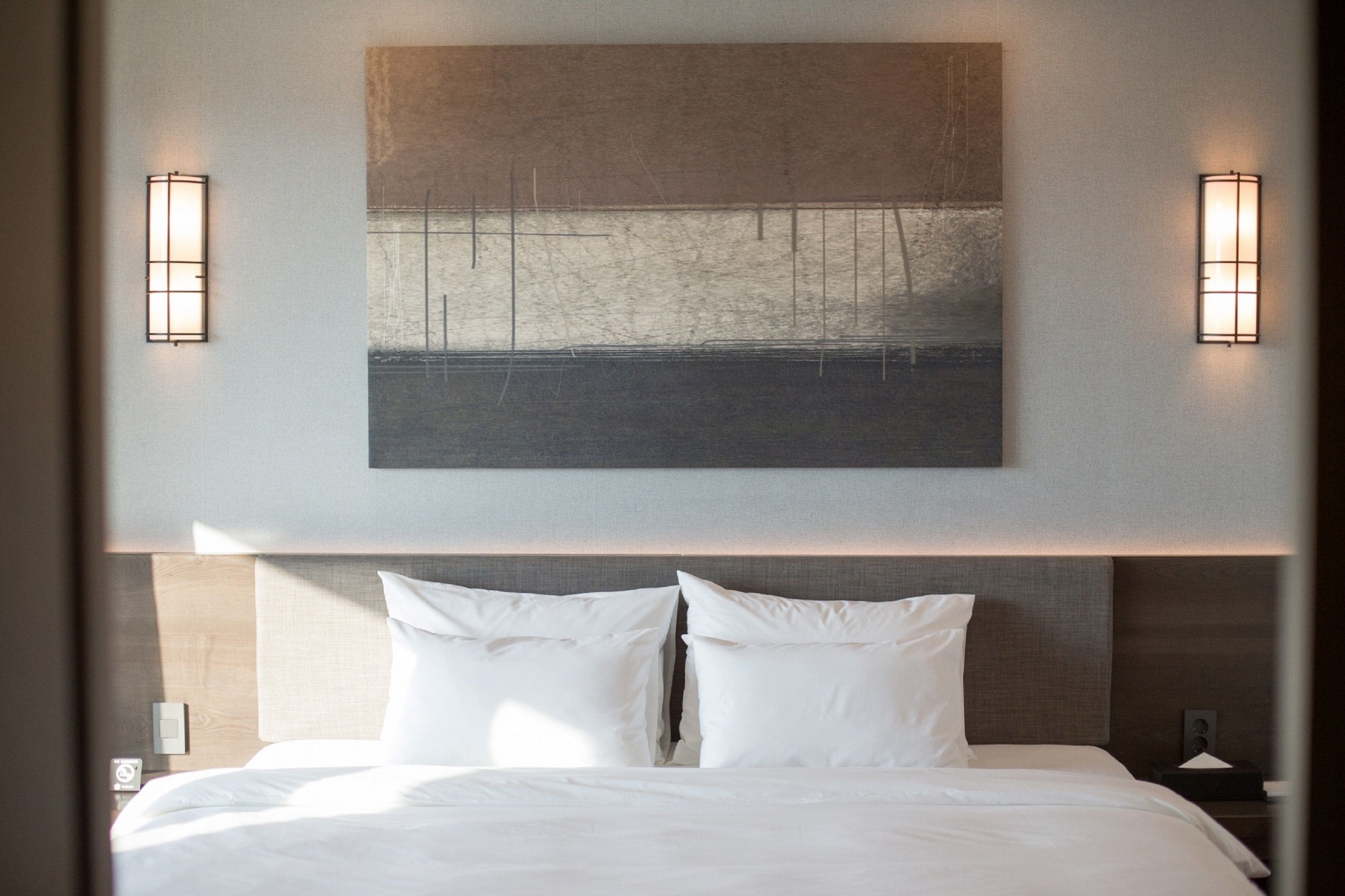 A hotel room with a large bed, two wall-mounted lights, and a painting above the bed.