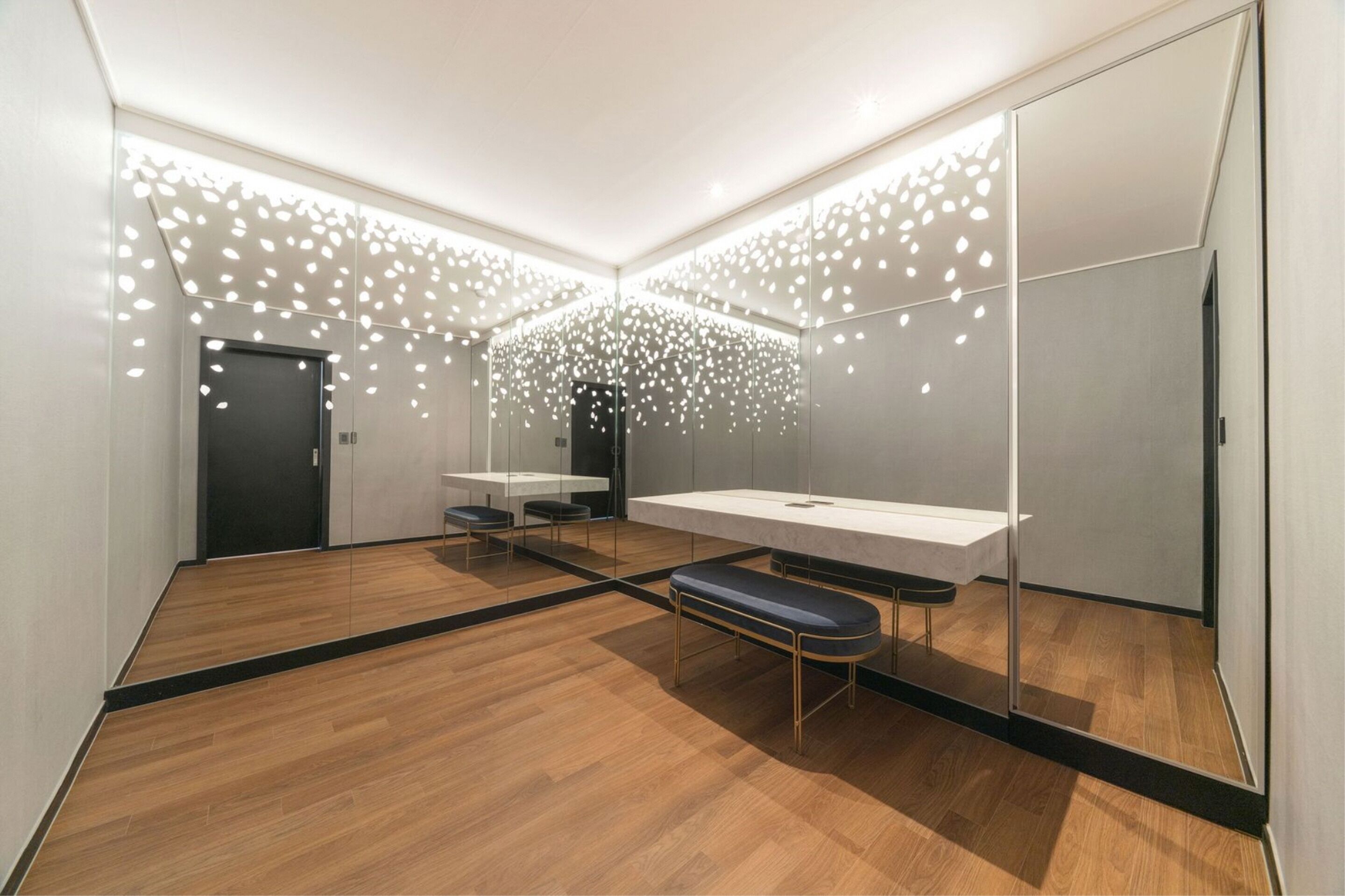A modern bathroom with a wooden floor, a bench, a sink, and a mirror.