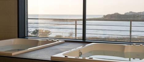 A bathroom with two large tubs and a view of the ocean through a large window.