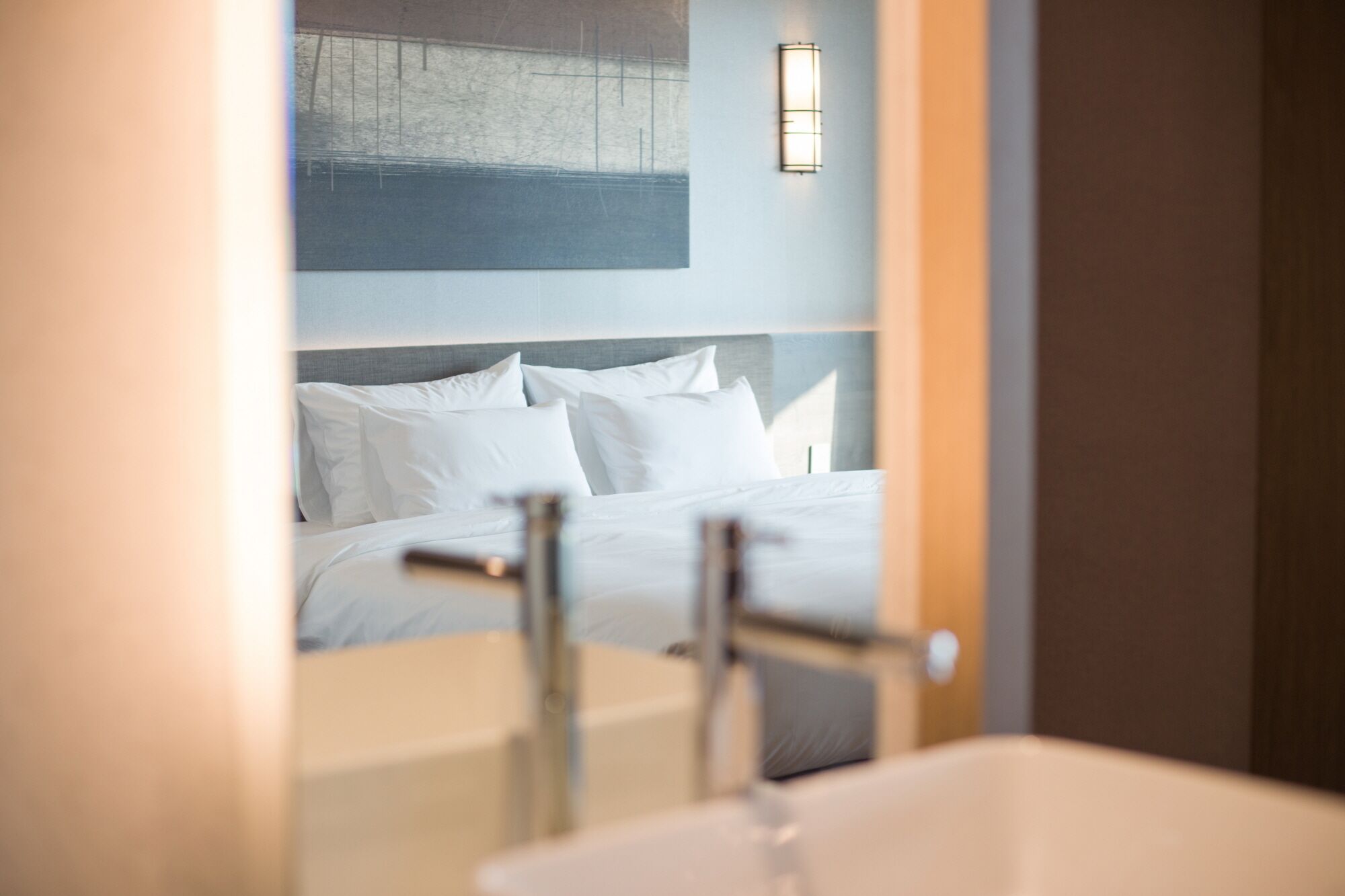 A hotel room with a bed, a nightstand, and a wall-mounted light fixture.