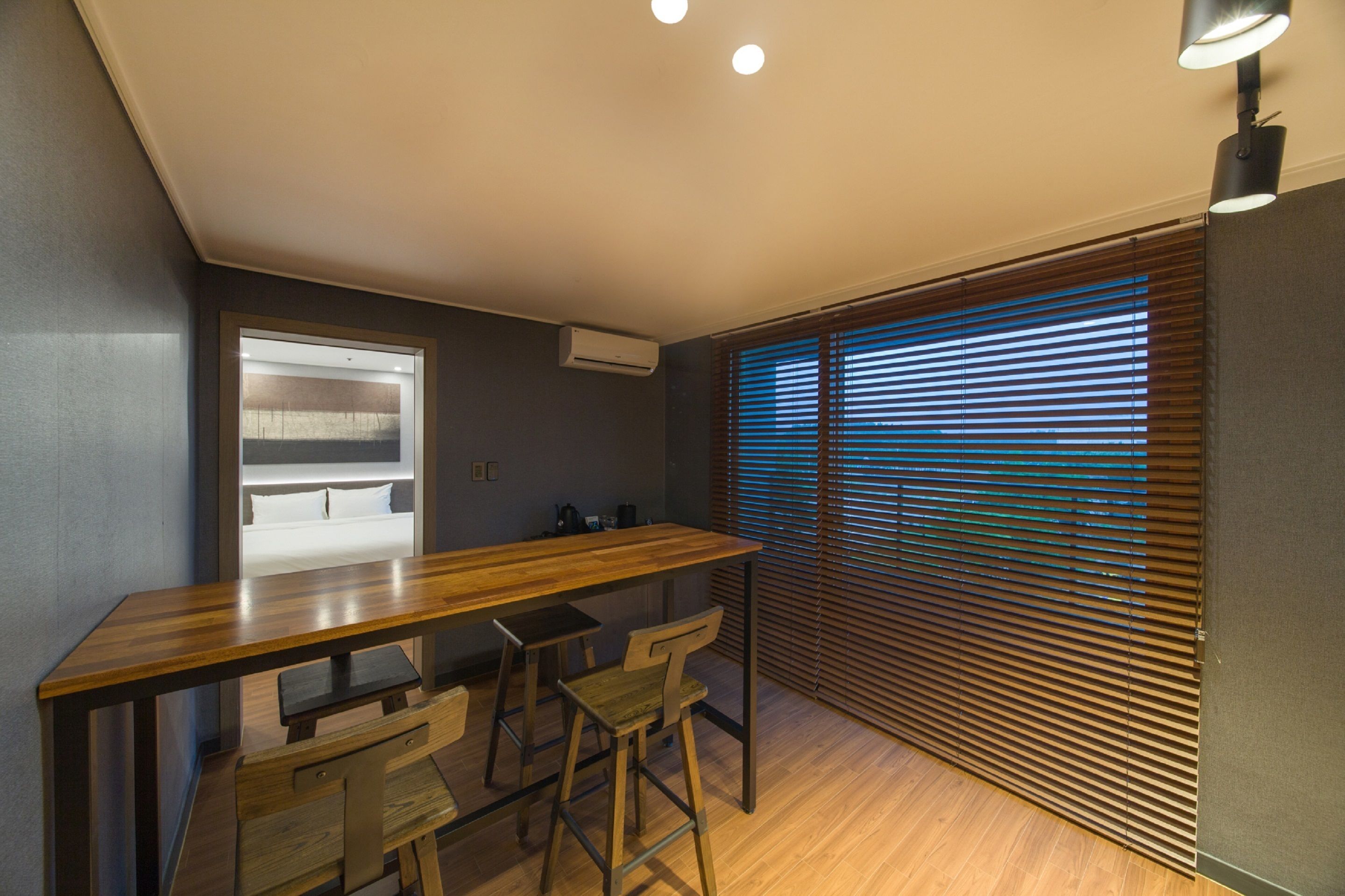 A modern kitchen with a wooden countertop, bar stools, and a window with blinds.