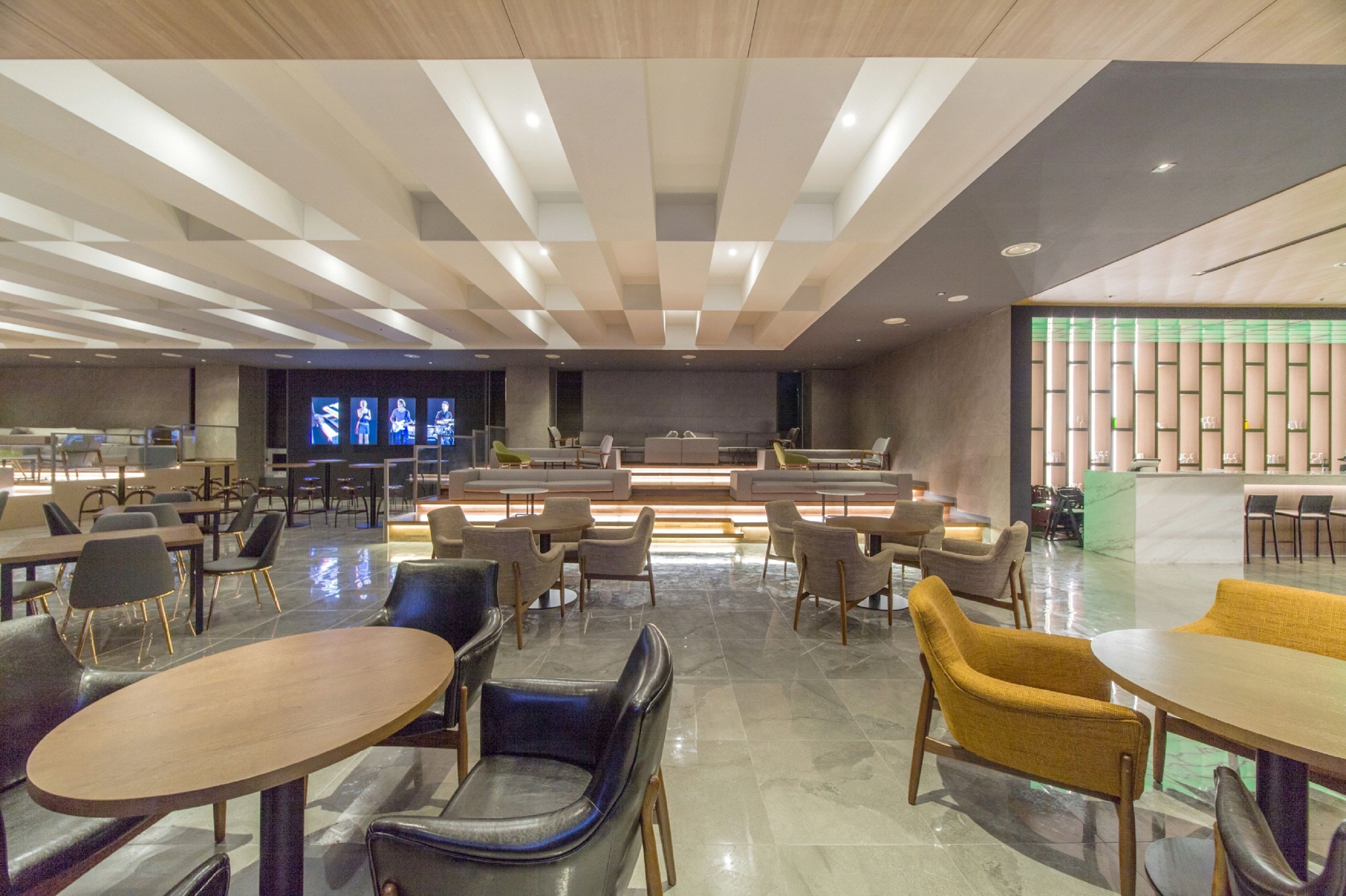 A modern hotel lobby with a central seating area, multiple tables, and a large screen displaying images.