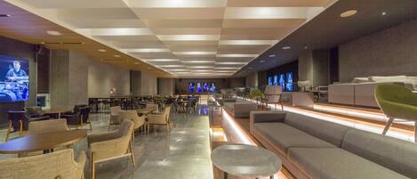 A modern lounge area with seating arrangements, a long counter, and a stage in the background.