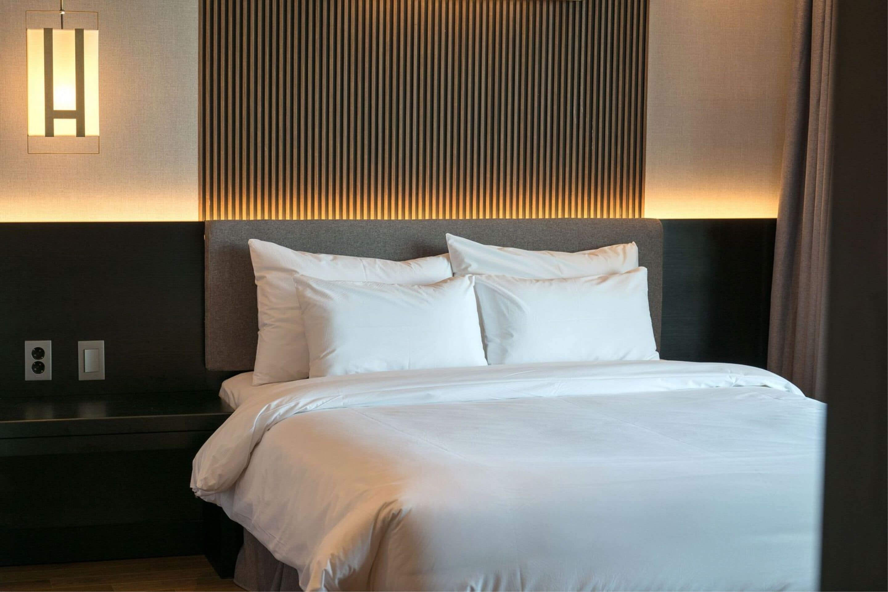 A neatly made bed with white linens in a hotel room.