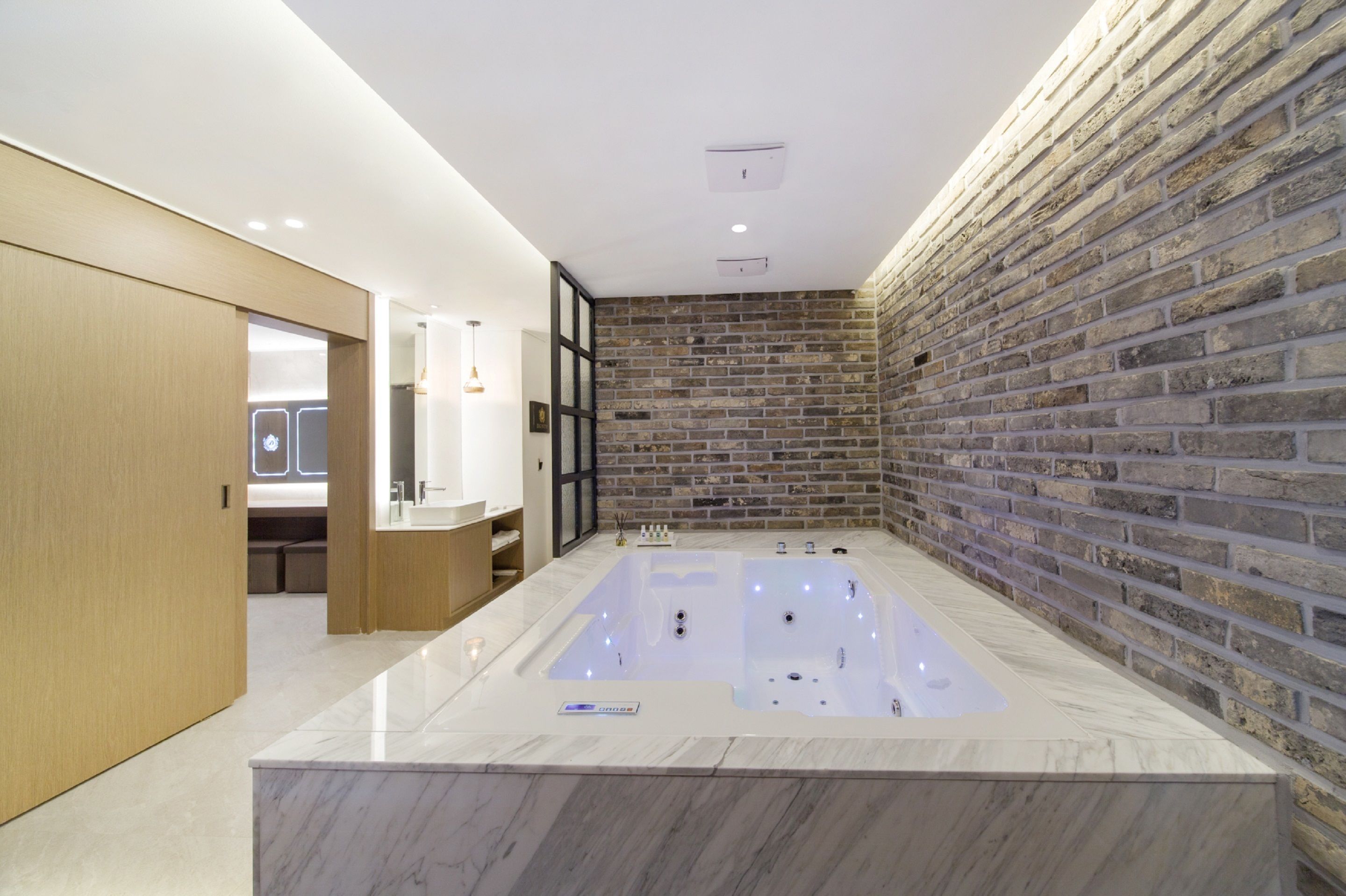 A modern bathroom with a large bathtub, wooden cabinets, and a brick wall.