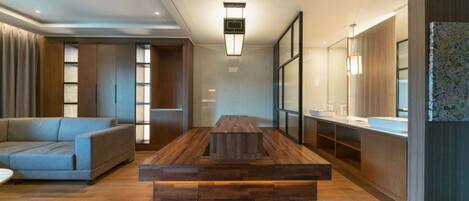 Uma sala de estar moderna com uma mesa de centro de madeira, um sofá cinza e uma área de cozinha com bancada e armários.