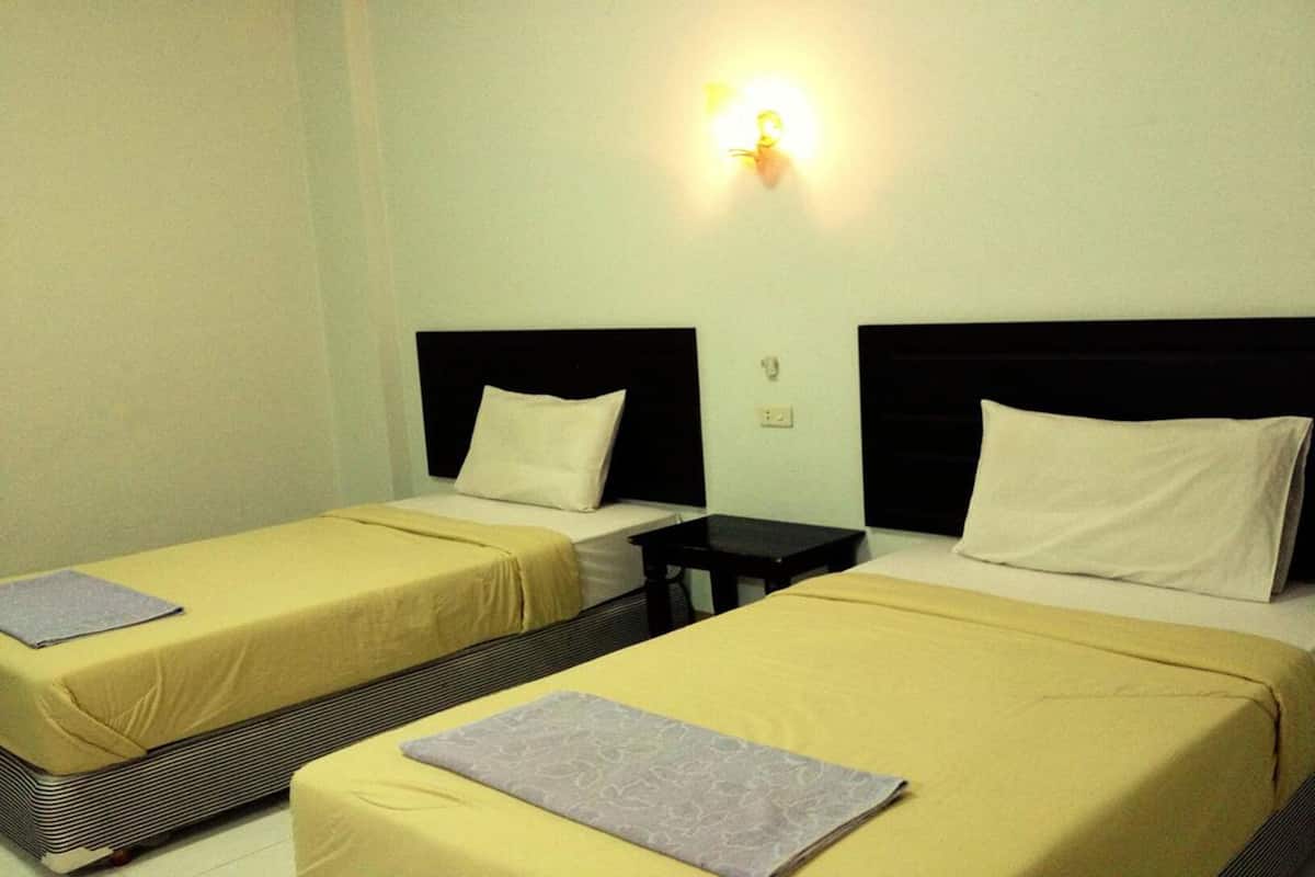 Habitación de hotel con dos camas individuales, cada una con una almohada y una mesita entre ellas.