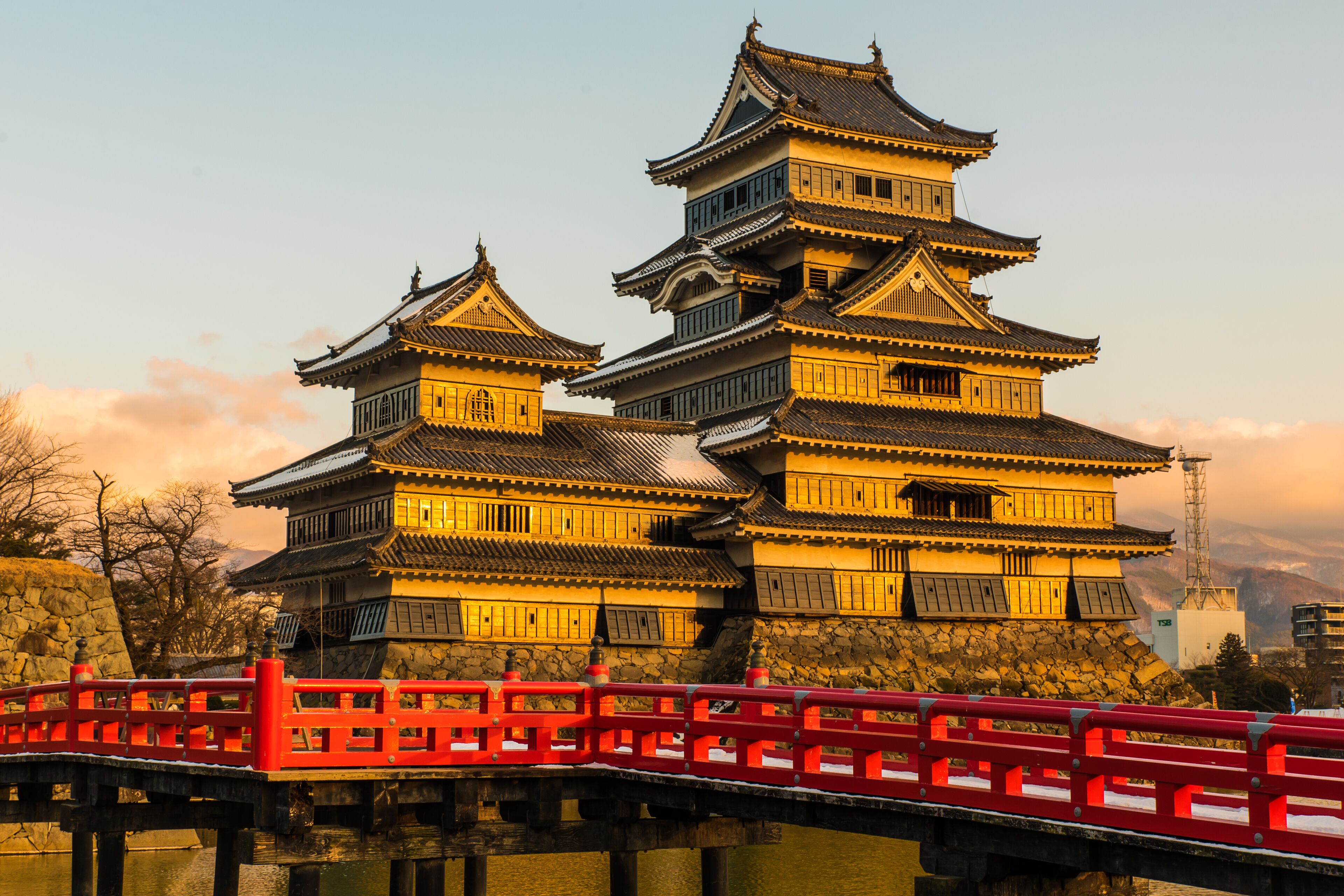 A traditional Japanese castle with multiple tiers and a red bridge in the foreground.