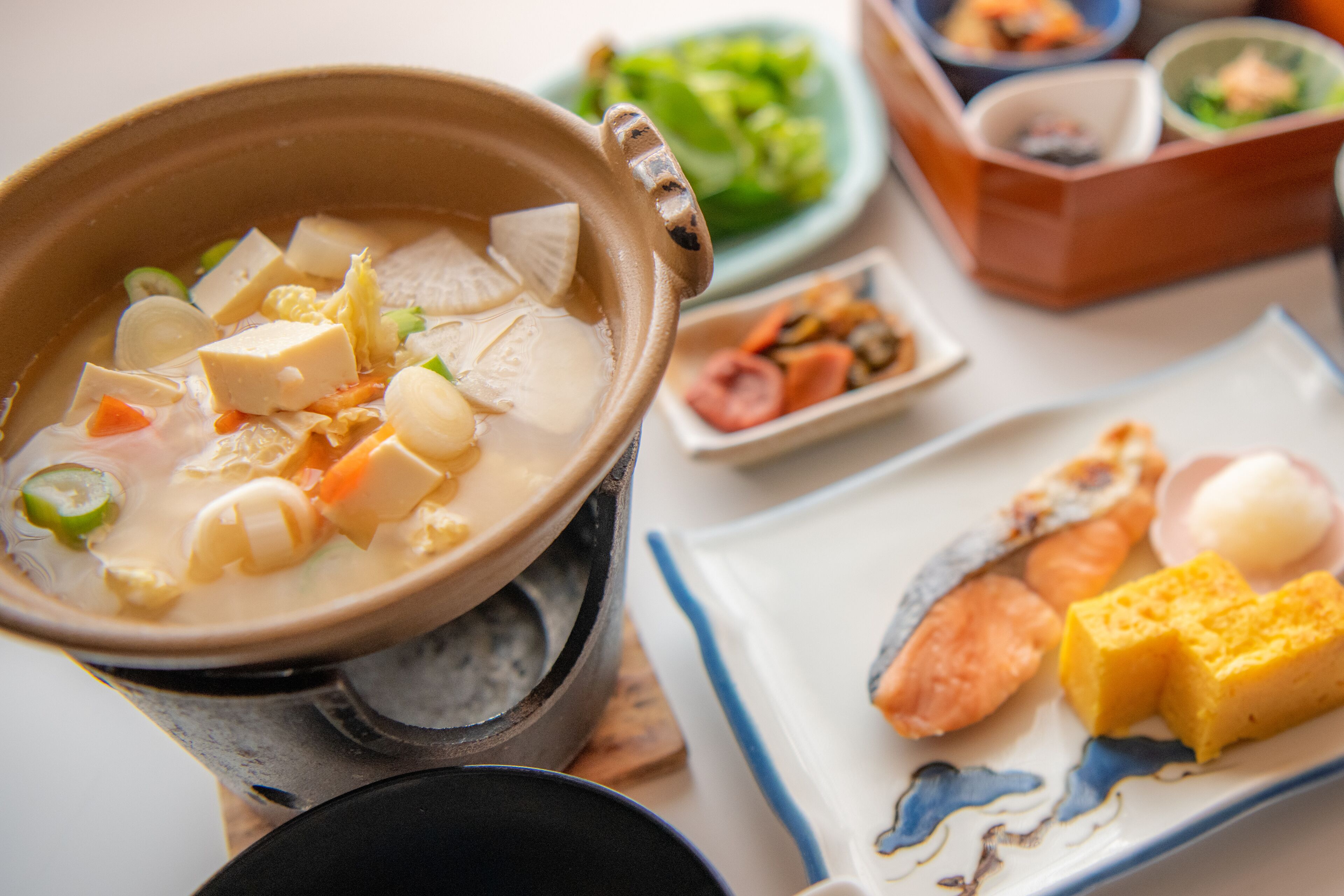Un bol de soupe contenant divers légumes et du tofu, accompagné d’une assiette composée de poisson, d’œuf et de légumes.