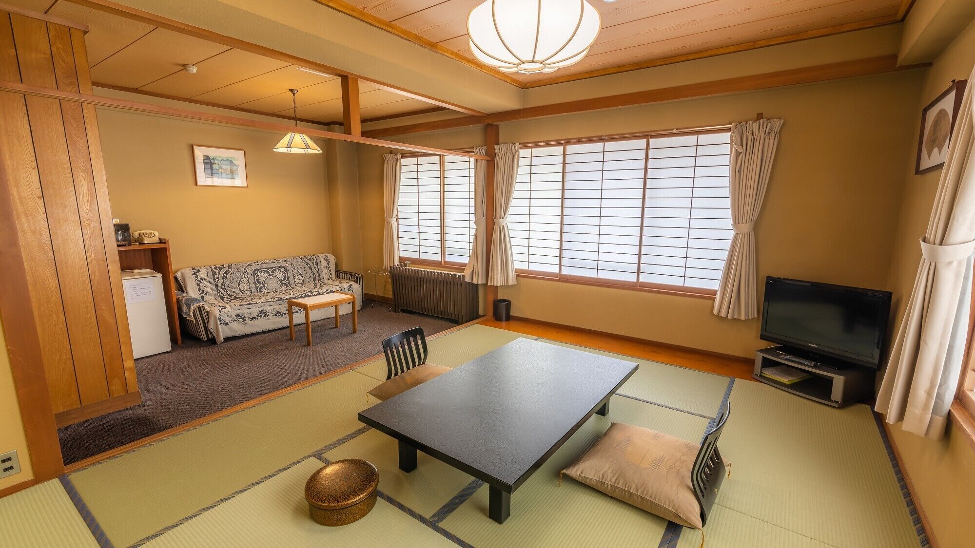 Una habitación japonesa tradicional con suelo de tatami, una mesa baja, un sofá, un televisor y un radiador.