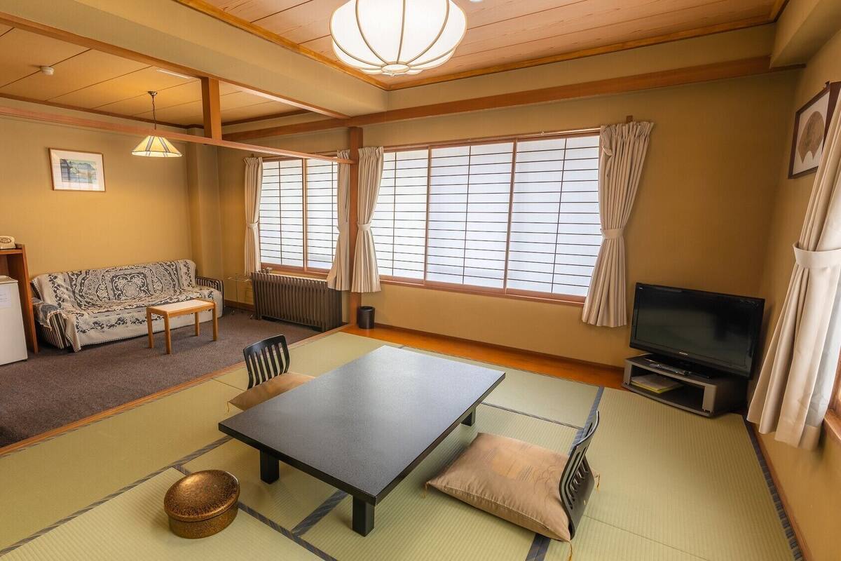 Ett traditionellt japanskt rum med tatamimattor på golvet, ett lågt bord, en soffa, en tv och ett element.